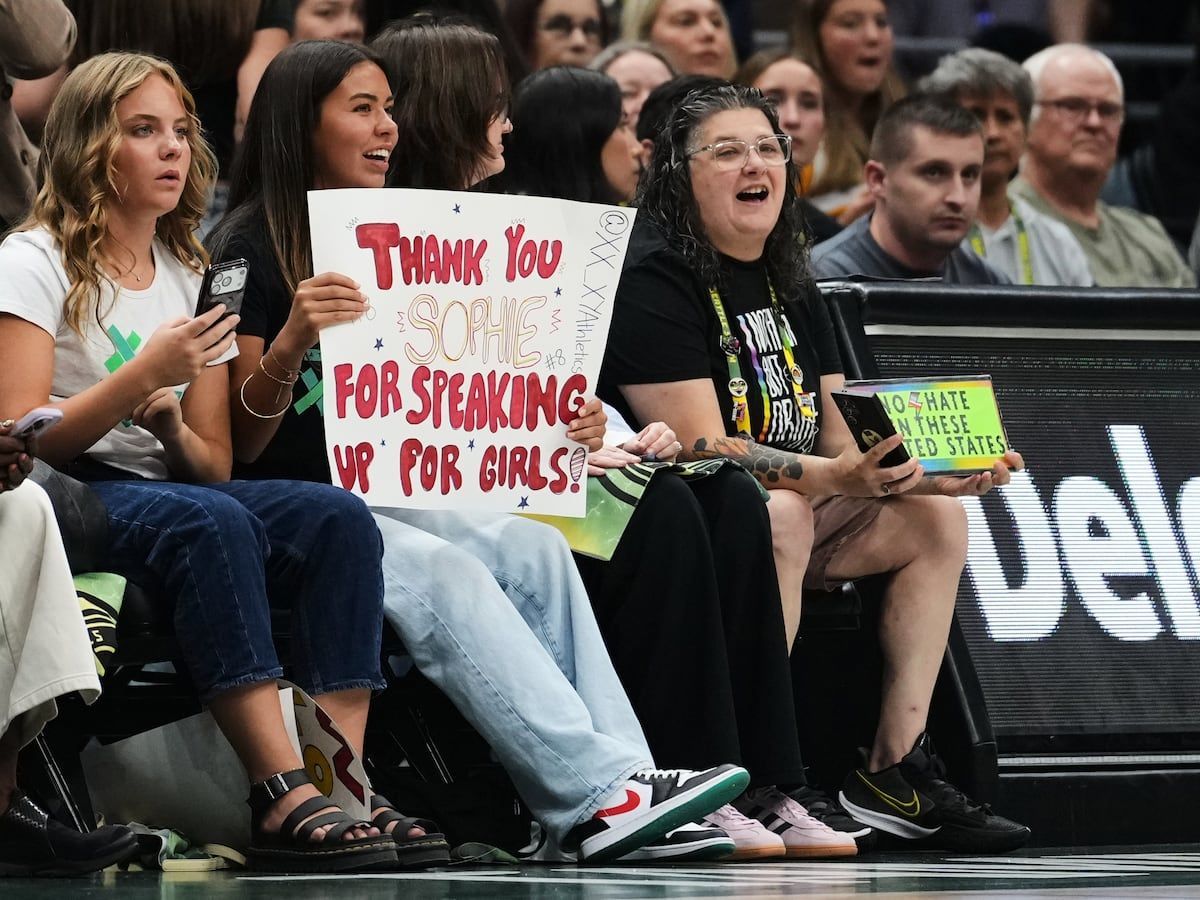 A fan holds a sign for Indiana Fever guard Sophie Cunningham in reference to her comments on transgender athletes as a fan wearing Seattle Storm gear holds a competing sign during the first half of a WNBA basketball game, Tuesday, July 28, 2026, in Seattle. - AP Photo/Lindsey Wasson
