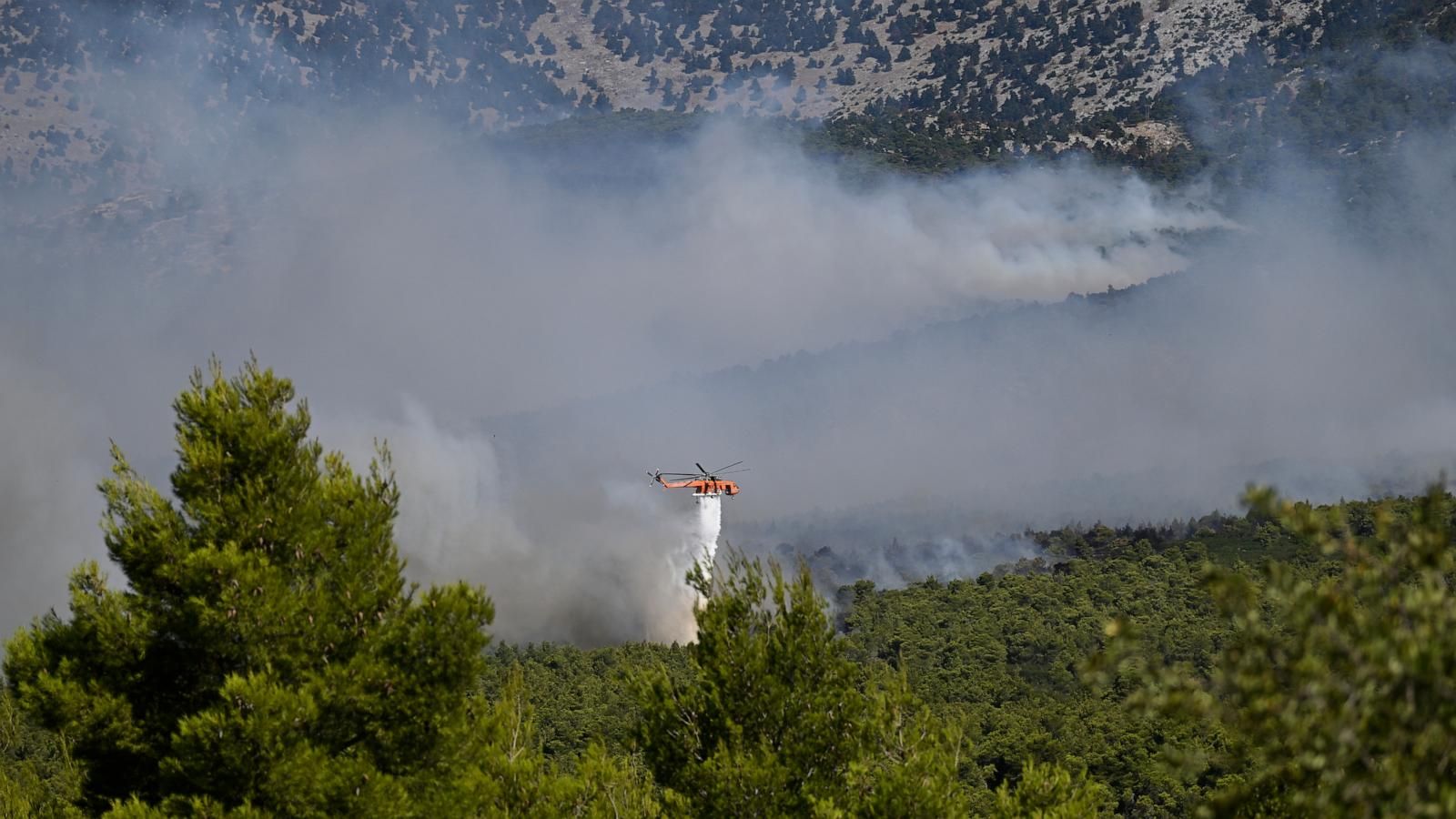 A firefighting helicopter drops water over a smoke-filled forest near Porto Germeno, northwest of Athens. - AP Photo/Michael Varaklas