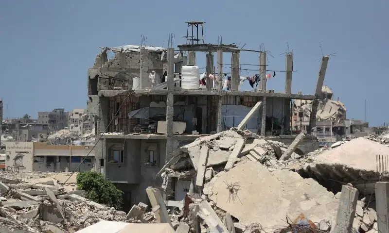 A Palestinian woman stands on the roof of a house damaged during the war, surrounded by destroyed buildings, in Gaza City, August 1. - AFP
