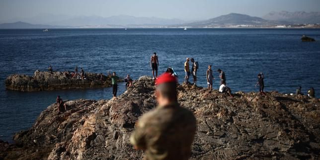A Spanish soldier stands before a group of migrants near the border crossing of the Spanish enclave of Ceuta, August 2, 2026. - lemonde.fr